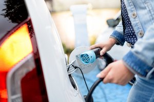 Eine Frau lädt ihr weißes Elektrofahrzeug mit einem schwarzen Kabel mit hellblauem Charging-Point auf.